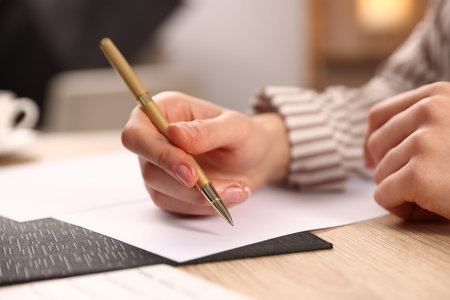 Woman writing on sheet of paper with pen at wooden table, closeup