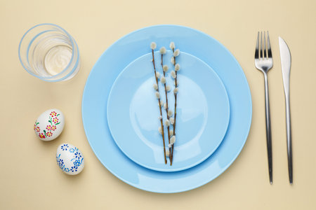 Easter celebration. Festive table setting with painted eggs, willow branches and cutlery on beige...