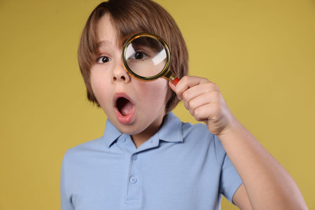 Surprised little boy with magnifying glass on yellow backgroundの写真素材