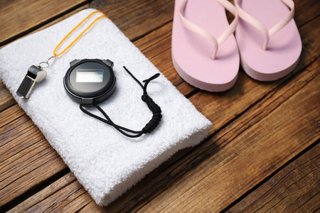 Towel, digital stopwatch, whistle and flip flops on wooden background, closeup. Swimming accessories