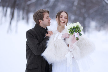 Happy newlywed couple with bouquet of flowers outdoors on winter day
