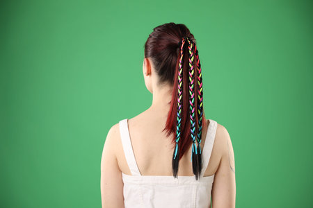 Woman with stylish braids on green background, back view