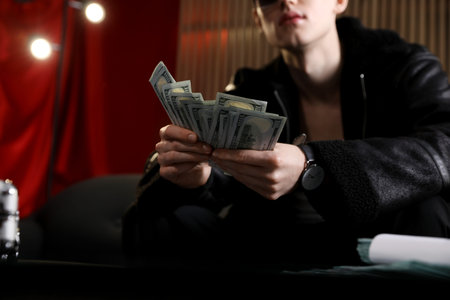 Young businessman in jacket with dollar banknotes on sofa indoors, closeupの写真素材