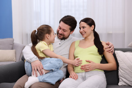 Pregnant woman, her husband and daughter on sofa at home