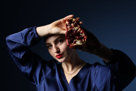 Beautiful woman with ripe pomegranate on blue backgroundの写真素材
