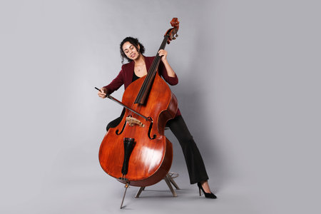 Woman playing double bass on gray background