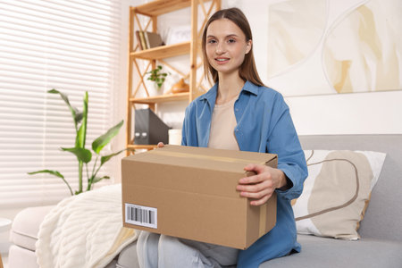 Woman with parcel on sofa at home. Space for text