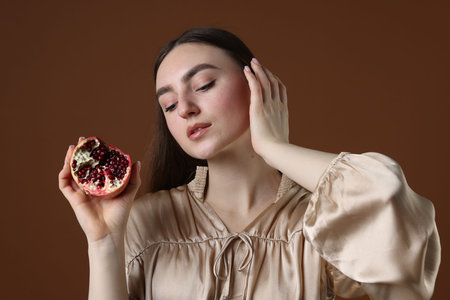 Beautiful woman with ripe pomegranate on brown backgroundの写真素材