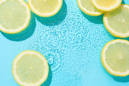 Lemon slices in water on light blue background, flat lay. Space for textの写真素材