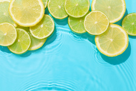Lemon and lime slices in water on light blue background, flat lay. Space for textの写真素材
