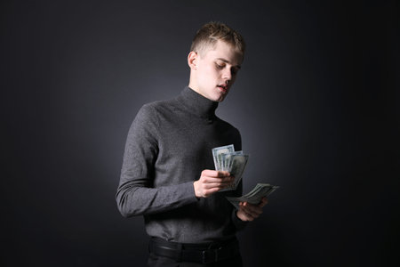 Young businessman counting money on dark background