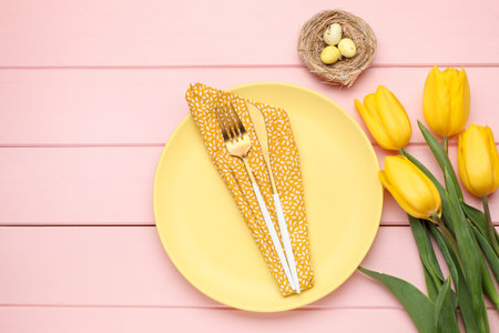 Easter celebration. Festive place setting with tulip flowers, cutlery and painted eggs on pink wooden table, flat lay with space for textの写真素材