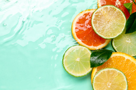Slices of citrus fruits and green leaves in water on turquoise background, flat lay. Space for textの写真素材