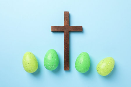Wooden cross and painted Easter eggs on light blue background, flat layの写真素材