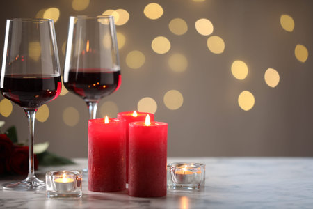 Burning candles and glasses of red wine on light marble table against gray background with blurred lights, closeup with space for text. Bokeh effectの写真素材