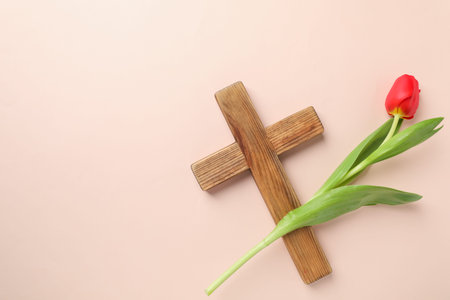 Easter attributes. Wooden cross and beautiful tulip on beige background, top view. Space for textの写真素材