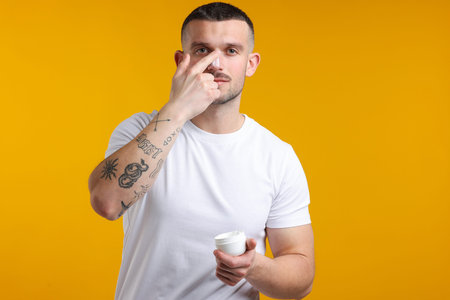 Man applying cream onto his face against yellow backgroundの写真素材