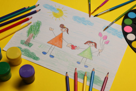 Child's drawing, paints and pencils on yellow background, above view