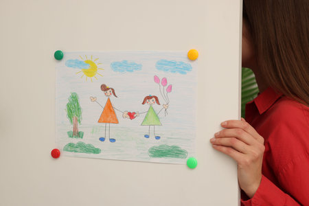 Woman near white cabinet with child's drawing indoors