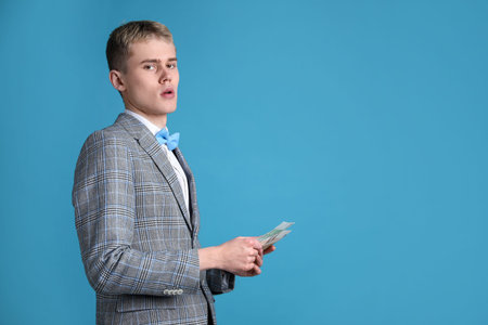 Young businessman in suit with banknotes on light blue background. Space for textの写真素材