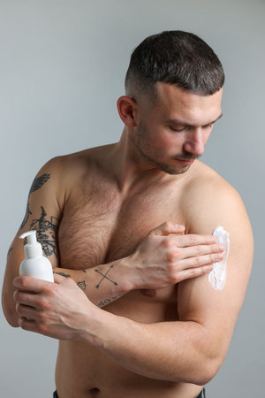 Man applying cream on his body against light gray background