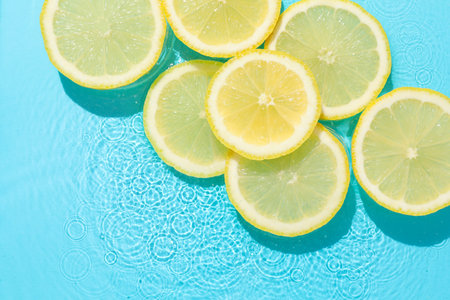 Lemon slices in water on light blue background, flat lay. Space for textの写真素材