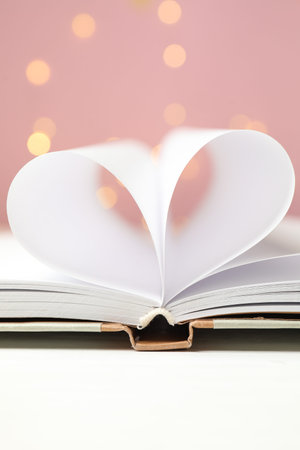 Love. Open book with pages folded in heart shape on white table against blurred lights, closeupの写真素材