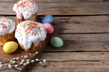 Delicious Easter cakes, painted eggs and willow branches on wooden table, space for text