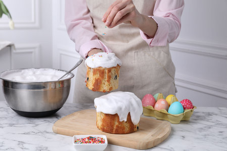 Woman decorating Easter cake with colorful sprinkles at white marble table indoors, closeupの写真素材