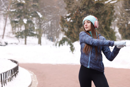 Woman with headphones stretching before run in winter park. Space for textの写真素材