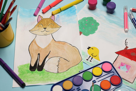 Child's drawings, felt-tip pens, paints and pencils on light blue background, above view