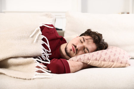 Man covered with plaid sleeping on couch at home