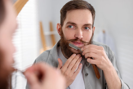 Handsome man shaving with straight razor near mirror at homeの写真素材