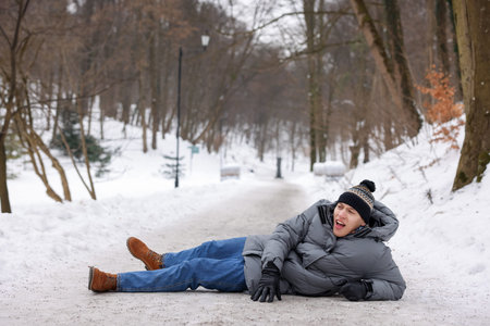 Young man fallen on slippery pathway covered in ice outdoors