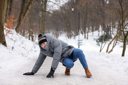 Young man fallen on slippery pathway covered in ice outdoorsの写真素材