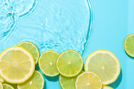 Lemon and lime slices in water on light blue background, flat lay. Space for text