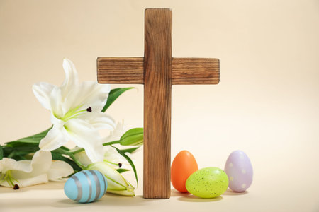 Easter. Wooden cross, painted eggs and beautiful lily flower on beige background, closeupの写真素材