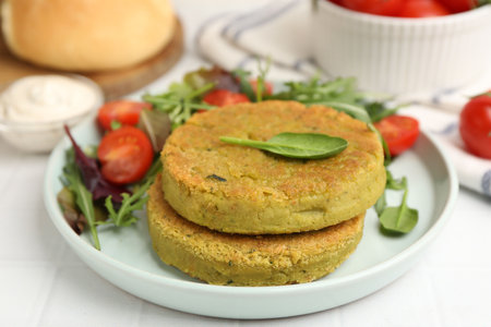 Tasty vegan patties with salad served on white tiled table, closeup