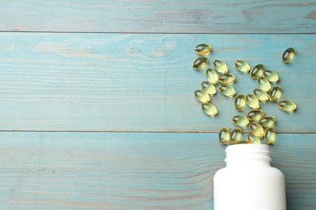 Medical bottle with golden gelatin capsules on blue wooden table, flat lay. Space for text