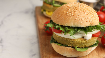 Tasty burger with vegan patty and vegetables served on white marble table, closeup. Space for textの写真素材