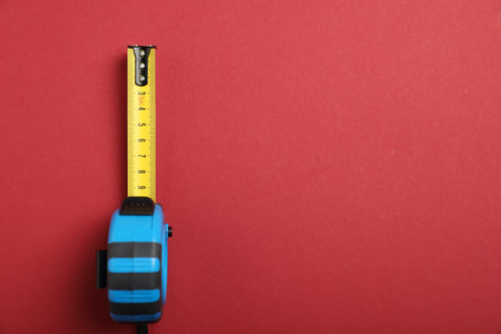 Measuring tape on red background, top view. Space for text