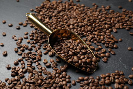 Coffee beans in scoop on black table, closeup
