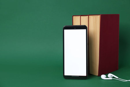 Smartphone with earphones and books on green background, closeup. Space for text