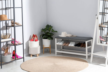 Shoe storage bench with different footwear, shelving unit, accessories, mirror and houseplant near light gray wall indoorsの写真素材