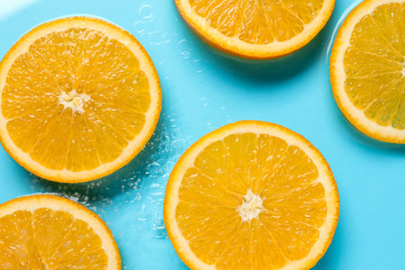Orange slices in water on light blue background, flat lay