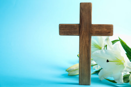 Easter. Wooden cross and beautiful lily flowers on light blue background, closeup with space for textの写真素材