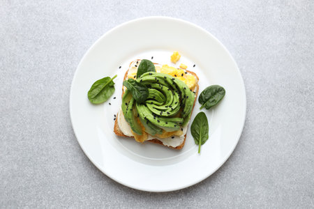 Tasty breakfast with avocado toast, scrambled eggs and spinach on light gray table, top view