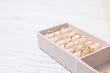 Beige tray with different gold rings on light wooden table, closeup. Space for text