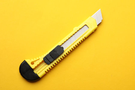 One sharp paper knife on yellow background, top view
