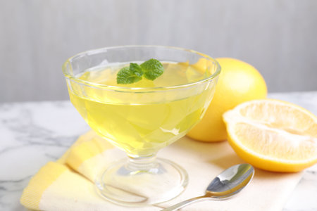Yellow jelly in dessert bowl, mint and fresh lemons on white marble table, closeupの写真素材